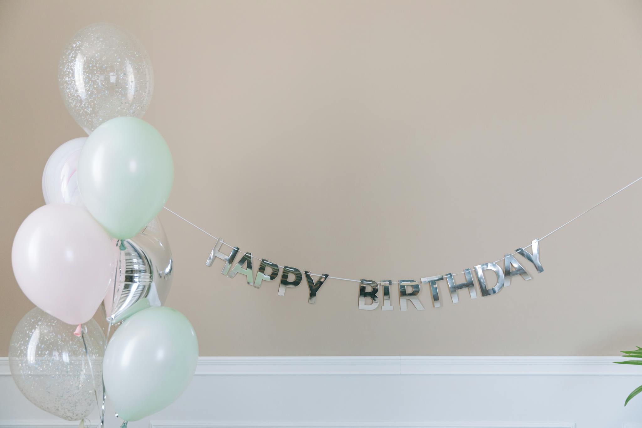 A minimalistic birthday setup featuring pastel balloons and a 'Happy Birthday' banner indoors.
