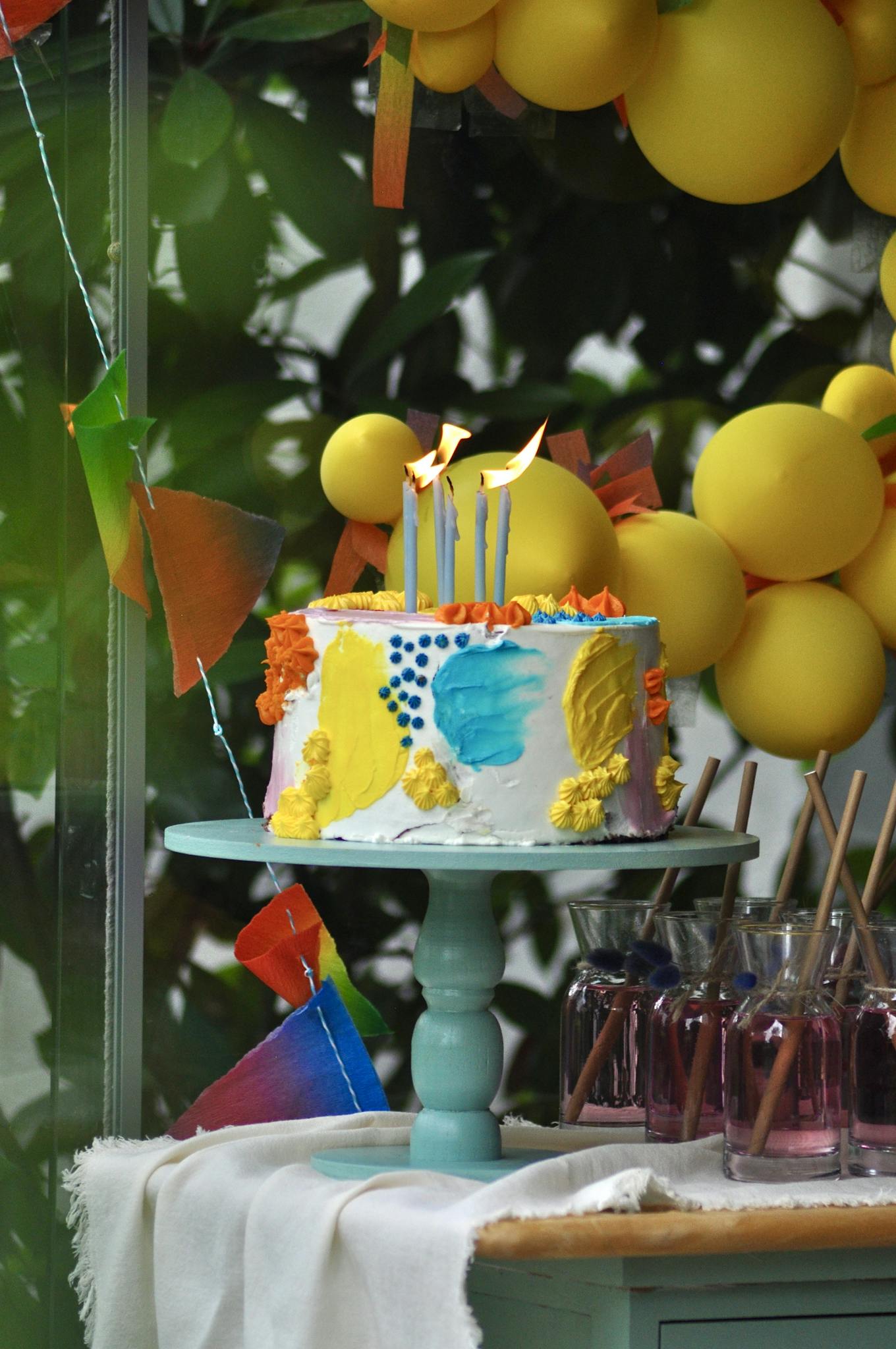 Colorful birthday cake with lit candles and yellow balloons, perfect for celebrations.